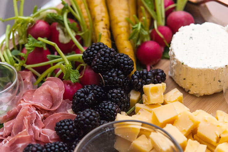 Prosciutto, cheese, blackberries, carrots and radishes on a tray.