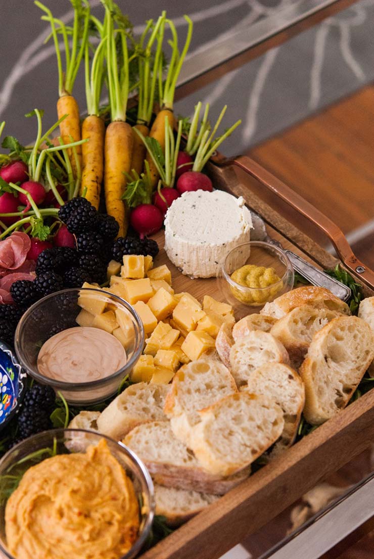 A tray with bread, carrots, prosciutto, cheese, blackberries and radishes.