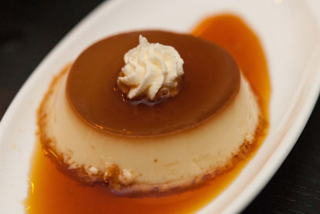 Flan on a white plate, topped with whipped cream.