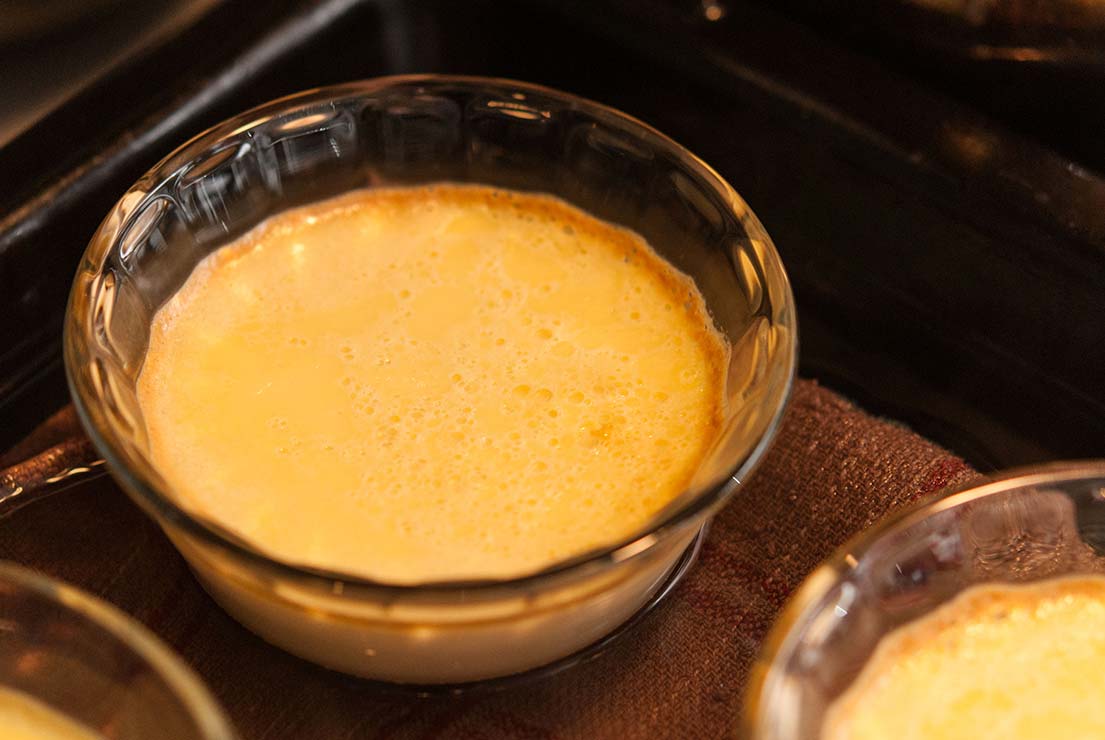 A flan with golden edges in a ramekin inside an oven.