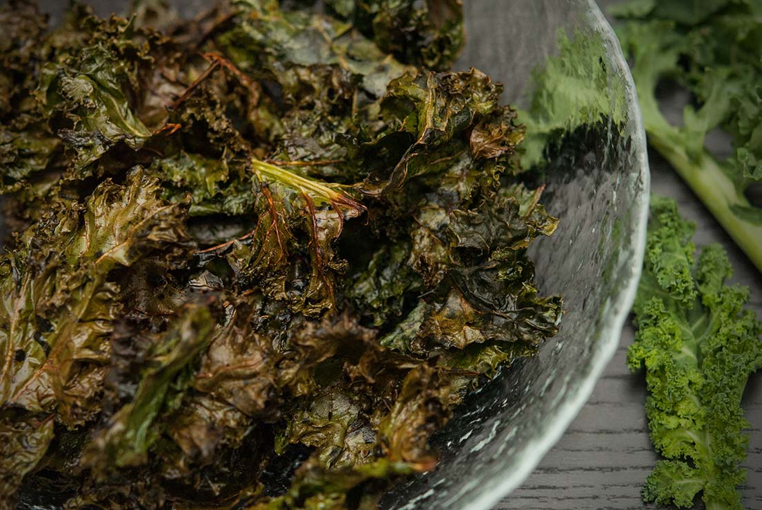 A bowl of kale chips on a black table.