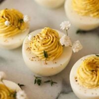 A marble slate with 5 deviled eggs, garnished with thyme and baby's breath.