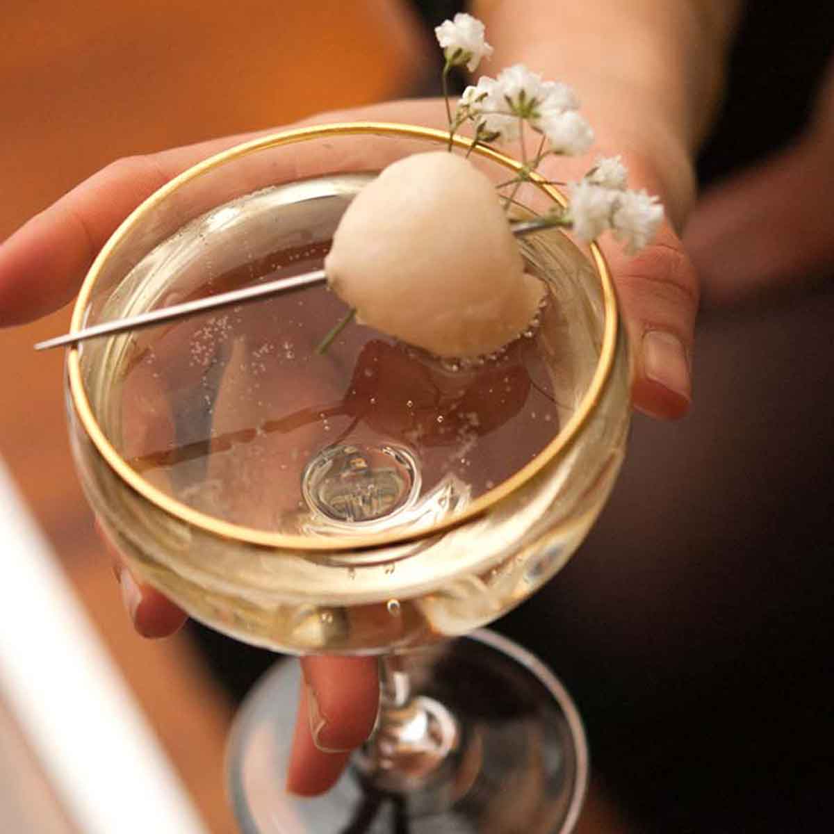 A hand holding a cocktail garnished with a lychee and baby's breath.