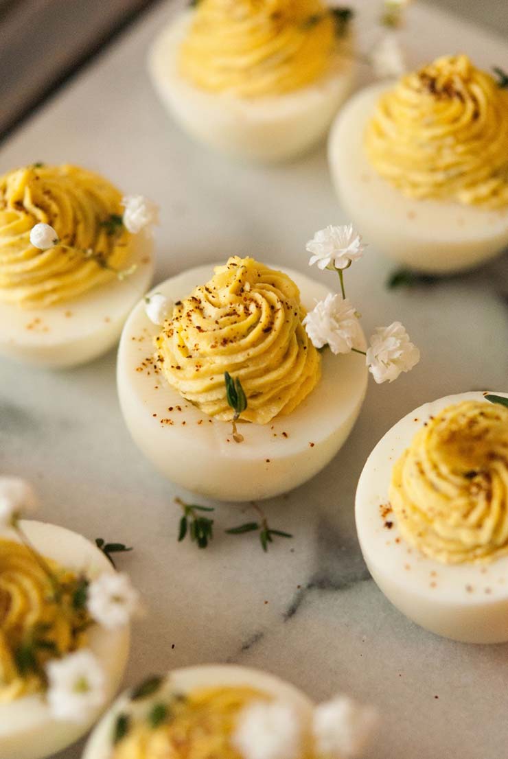 7 deviled eggs on a marble plate, garnished with baby’s breath and a few leaves of thyme.