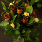 A “bouquet” of bacon roses in a vase with leaves and yellow spray roses.