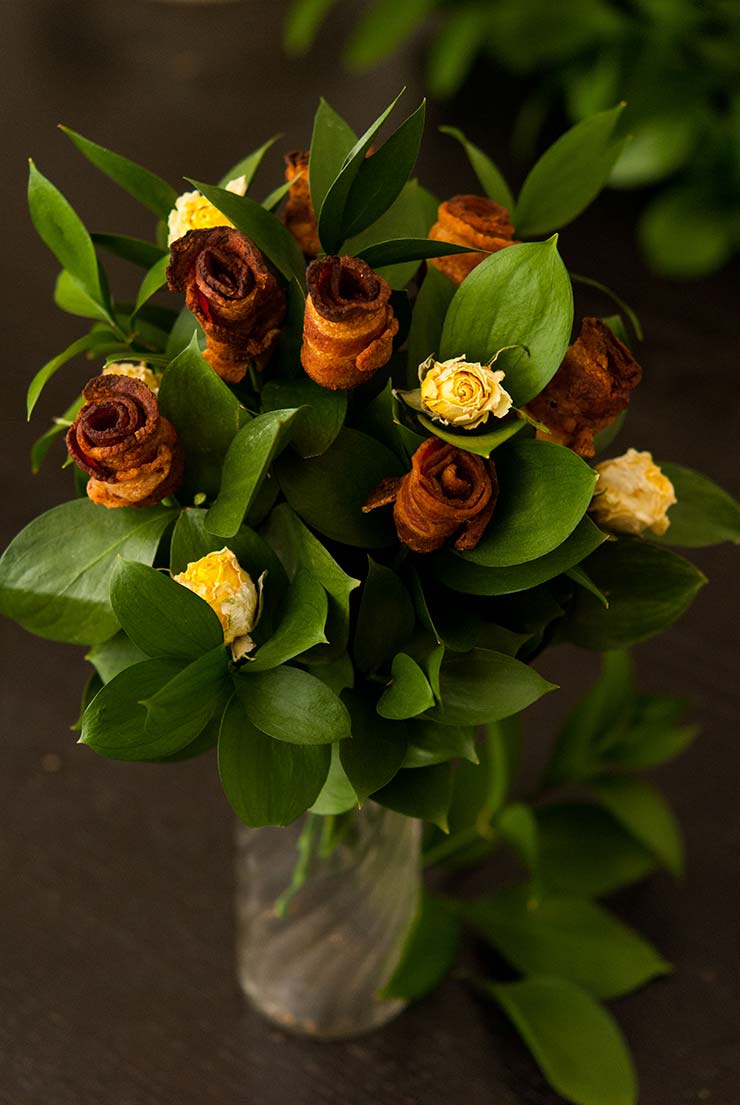 A bacon rose bouquet with yellow roses on a dark table.