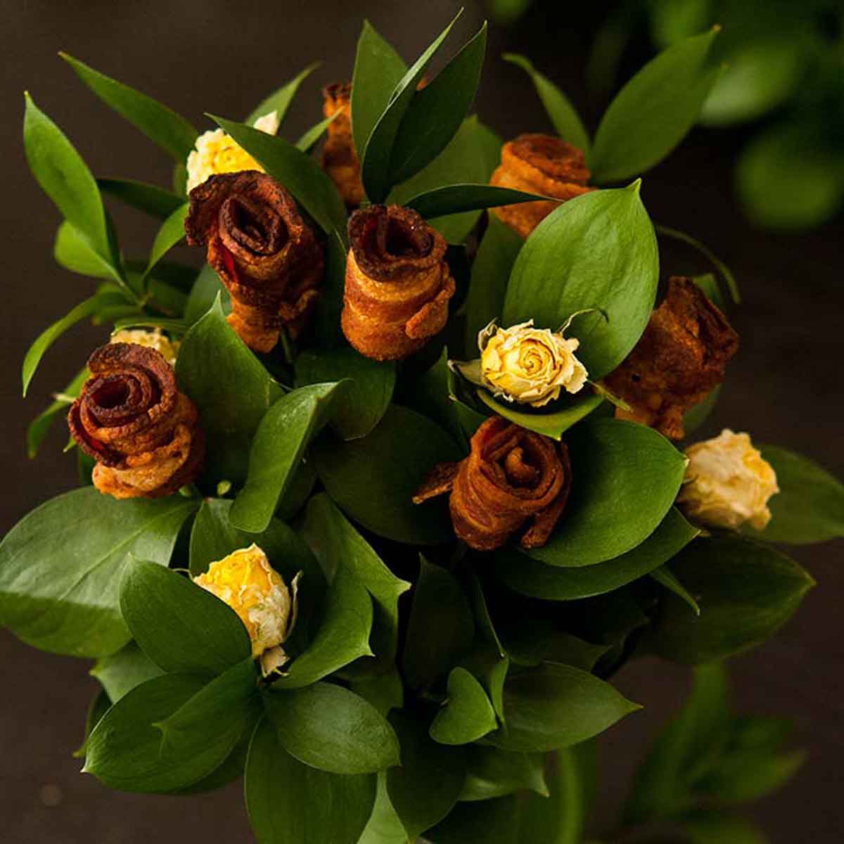 A bacon rose bouquet with yellow roses on a dark table.