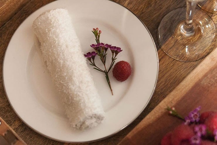 A small plate holding a rolled towel with a tiny flower and raspberry on a wooden tray.