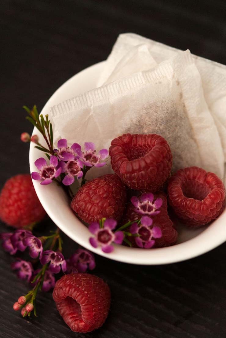 A cocktail garnished with small flowers and two raspberries, pierced with a cocktail pin.