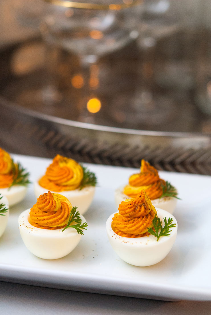 6 2-tone deviled eggs on a white plate, garnished with parsley, in front of a metal serving tray.