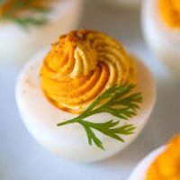 A yellow and orange deviled egg, garnished with a sprig of dill on a marble plate.