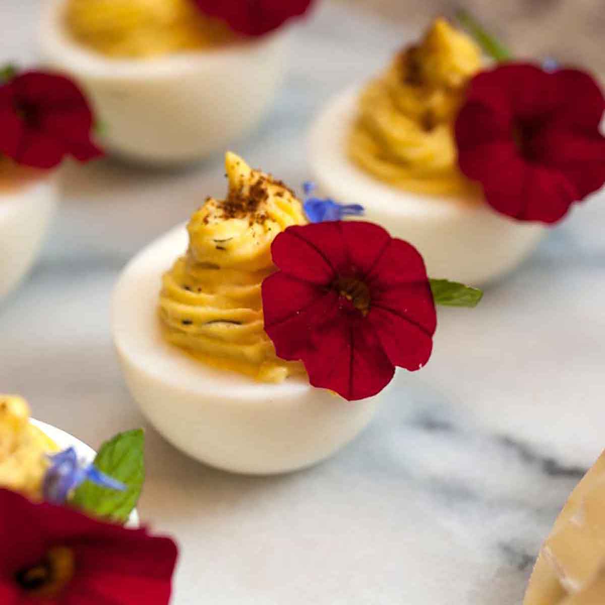 5 deviled eggs, garnished with red flowers on a marble board.