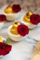 5 deviled eggs, garnished with red flowers on a marble board.