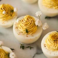 5 deviled eggs on a marble plate, garnished with baby’s breath and a few leaves of thyme.