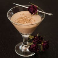 A smal cocktail, garnished with a single rose, with roses at its base.