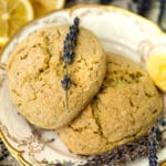 Two scones on plates with gold edges with fresh lavender placed on top, beside 2 cut lemons and a bunch of fresh lavender.