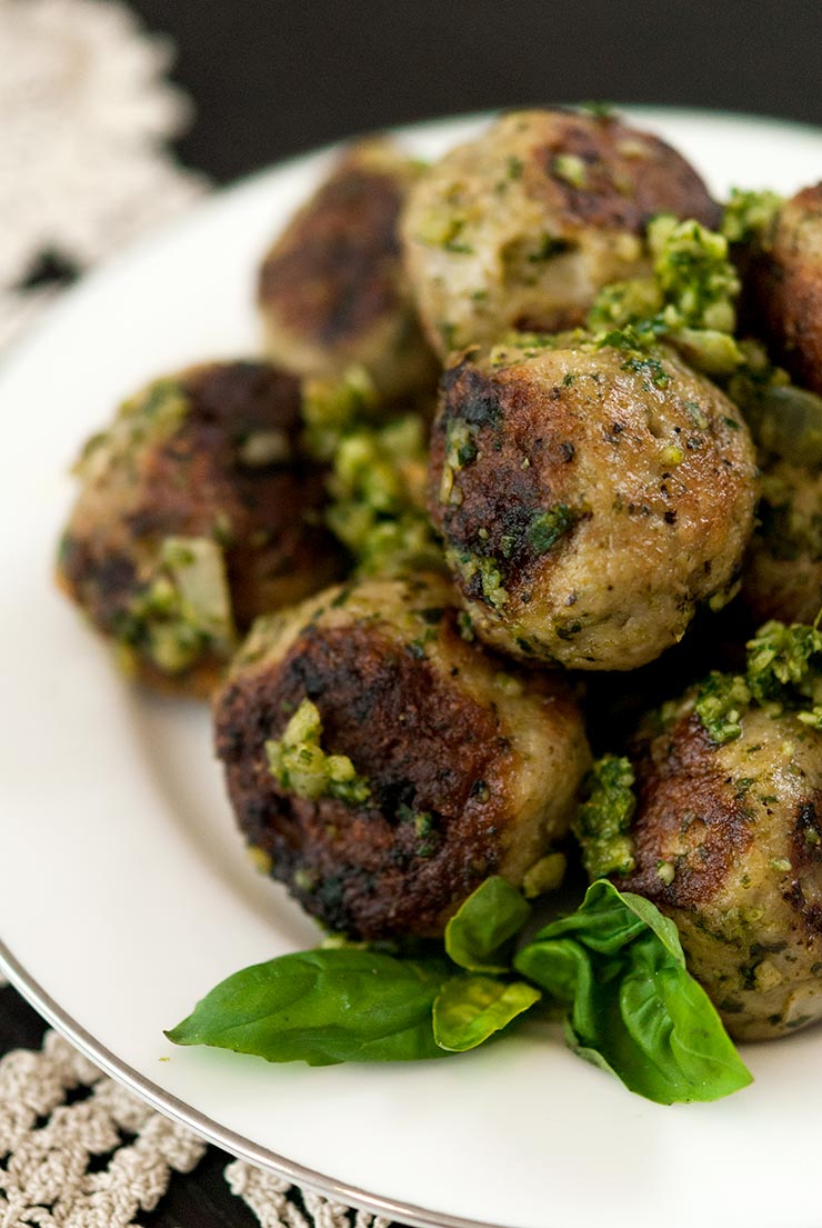 Pesto covered meatballs on a plate, garnished with basil.