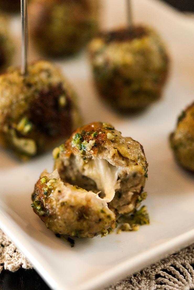 These incredible Italian turkey meatballs with homemade pesto and mozzarella will become everyone’s favorite appetizer at the party! This recipe is so simple and SO delicious! With melted cheese centers and that fresh, Italian pesto flavor, these perfect little appetizers make such an enticing hors d'oeuvre. They’re also gluten-free! #appetizers, #gluten-free, #pesto, #meatballs A meatball cut in half with melted cheese inside, on a plate with 3 other meatballs.