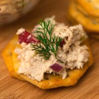 A cracker with chicken salad on a wooden plate.