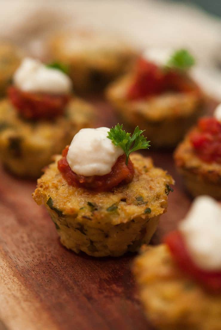 6 cauliflower cakes on a wooden board, topped with marinara, cream, and a little fresh parsley.