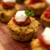 A cauliflower appetizer topped with tomato, cream and parsley beside 4 others on a wooden tray.