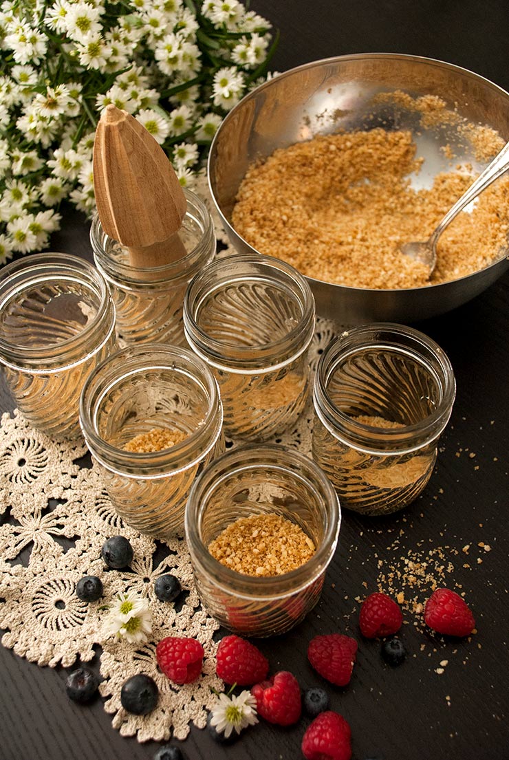 This no-bake vanilla cheesecake mousse is dreamy, creamy and layered with blueberries, raspberries and a scrumptious Nilla Wafer crumble! #cheesecake, #july4thfood, #mousse, #vanillacheesecake, #nobake, #dessert via @shekeepsalovelyhome 6 mason jars with cookie crumbles on the bottom on top of a lace cloth beside a bowl of cookie crumbles and a bouquet of daisies.