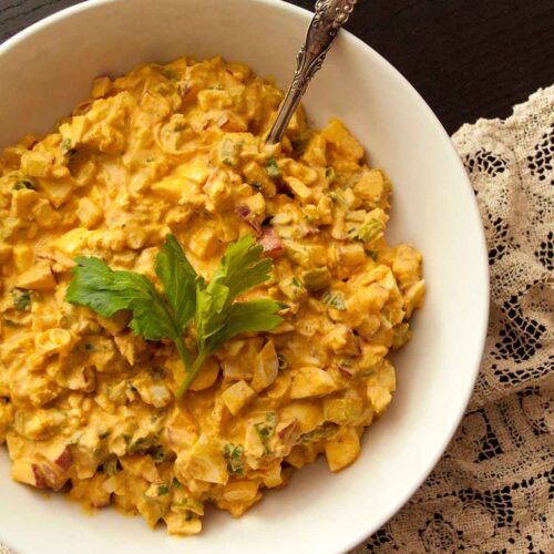 A bowl of spicy egg salad on a lace tablecloth with an antique spoon.