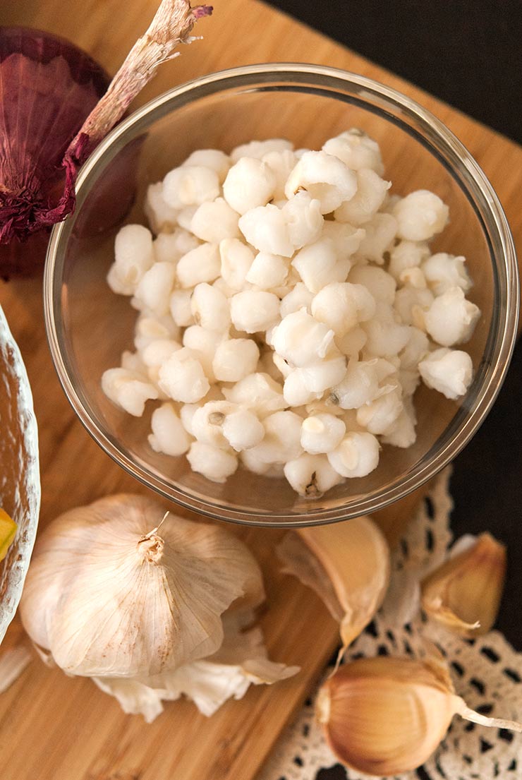 A bowl of hominy on a wooden board beside garlic.