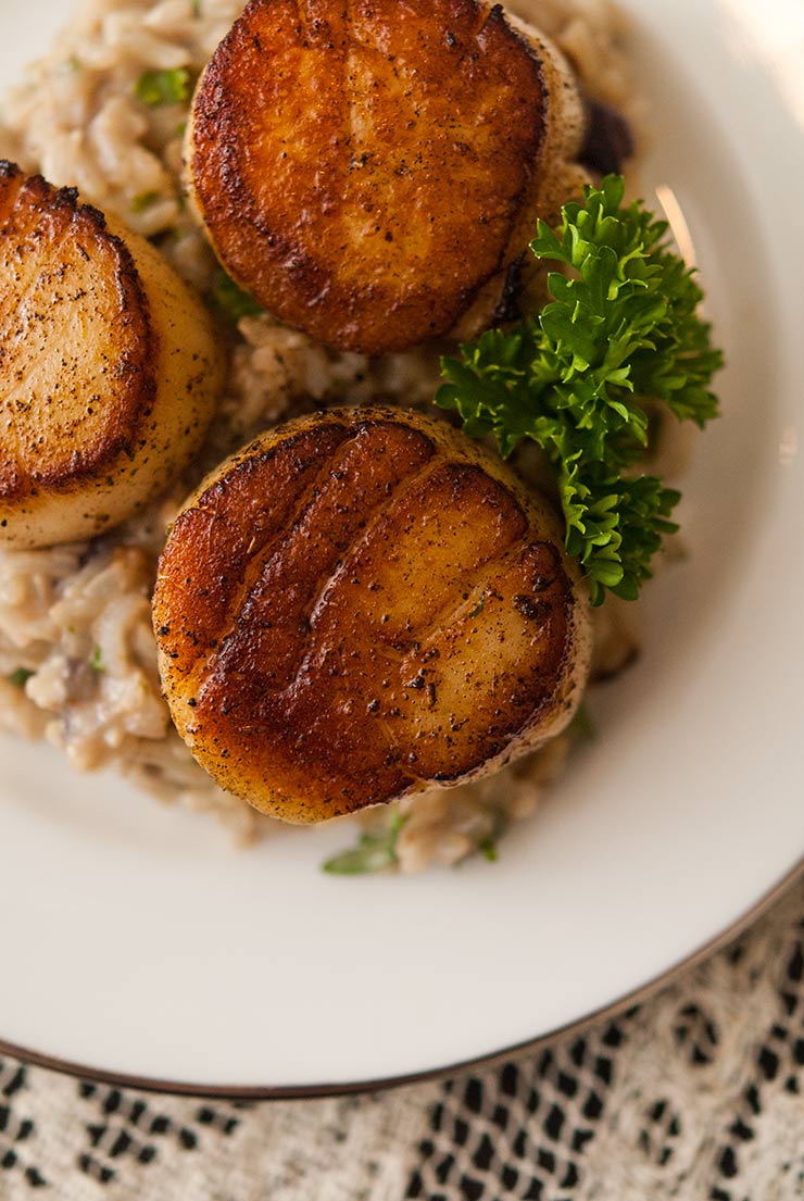 3 large seared scallops on a plate with rice, garnished with parsley.
