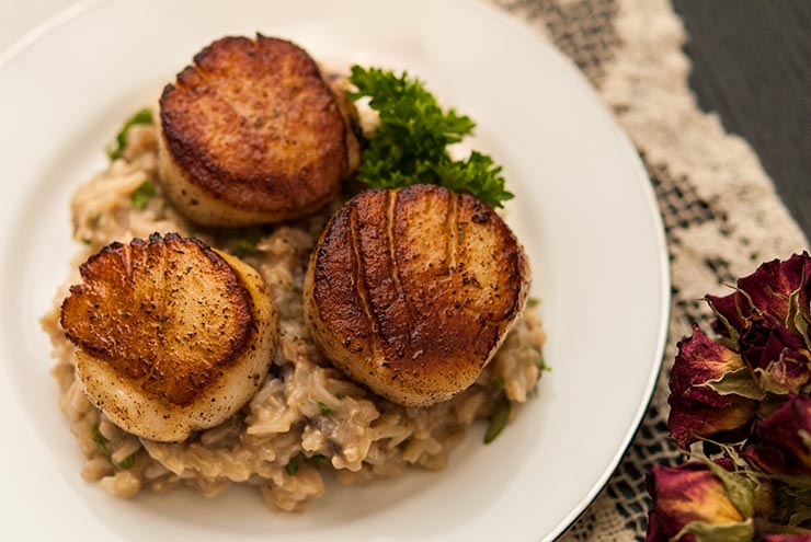 3 large seared scallops on a plate with rice, garnished with parsley, on top of a lace table cloth.