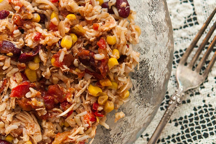 This Santa Fe chicken is packed with 7 different veggies, spiced with zesty, Tex-Mex flavors and serves at least 6 happy cowboys. It's also gluten-free! #glutenfree #mexican #recipe #easydinner #crockpot #crockpotrecipes A bowl of Santa Fe Chicken on a lace table cloth.