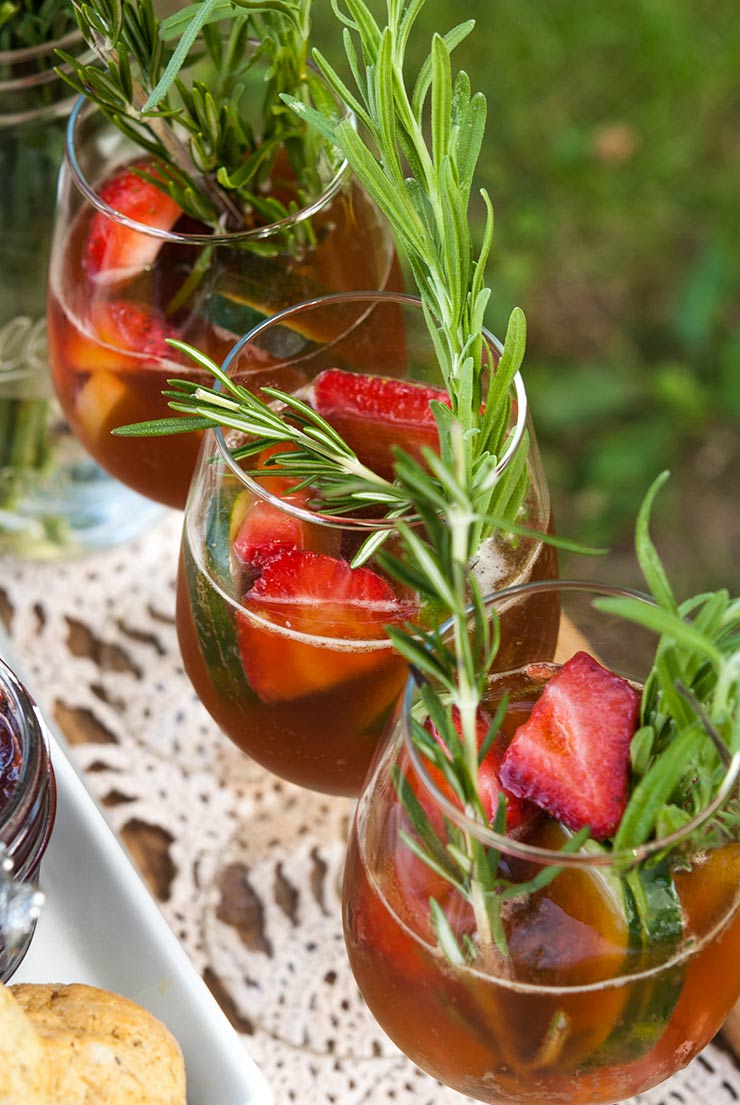 3 strawberry Pimm’s Cup cocktails, garnished with herbs and fruits on a lacy edge of a tray.