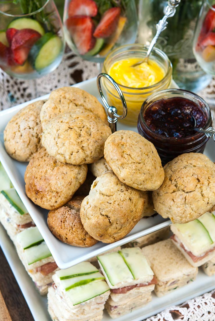 A appetizer tier with scones on top and cucumber sandwiches on the bottom, with cocktail glasses beside it.