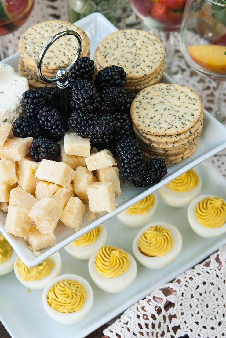 2 appetizer tiers. One with cheese, blackberries and crackers, and the one below, with deviled eggs.