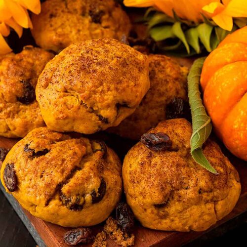 Pumpkin scones beside a small pumpkin and sunflower on a wooden board.