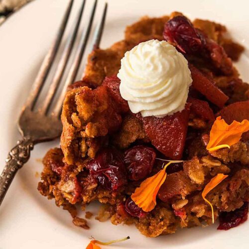 Cranberry apple crisp on a plate, topped with whipped cream and sprinkled with marigold flower petals.