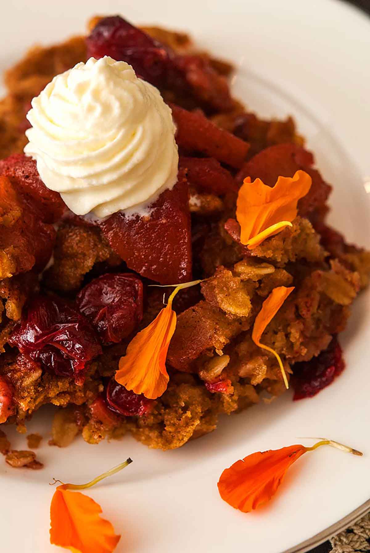 Cranberry apple crisp on a plate, topped with whipped cream and sprinkled with marigold flower petals.