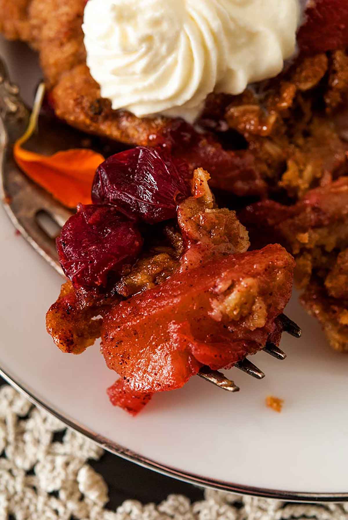 This fantastically tasty dessert is sweet, tart, crispy, chewy and crunchy! It’s so incredibly easy to make and can be made vegan! #desserts, #falldesserts, #appledessert, #applerecipes, #fallrecipes, #thanksgiving, #apples, #shekeepsalovelyhome Cranberry apple crisp on a fork with a few sprinkled marigold petals.