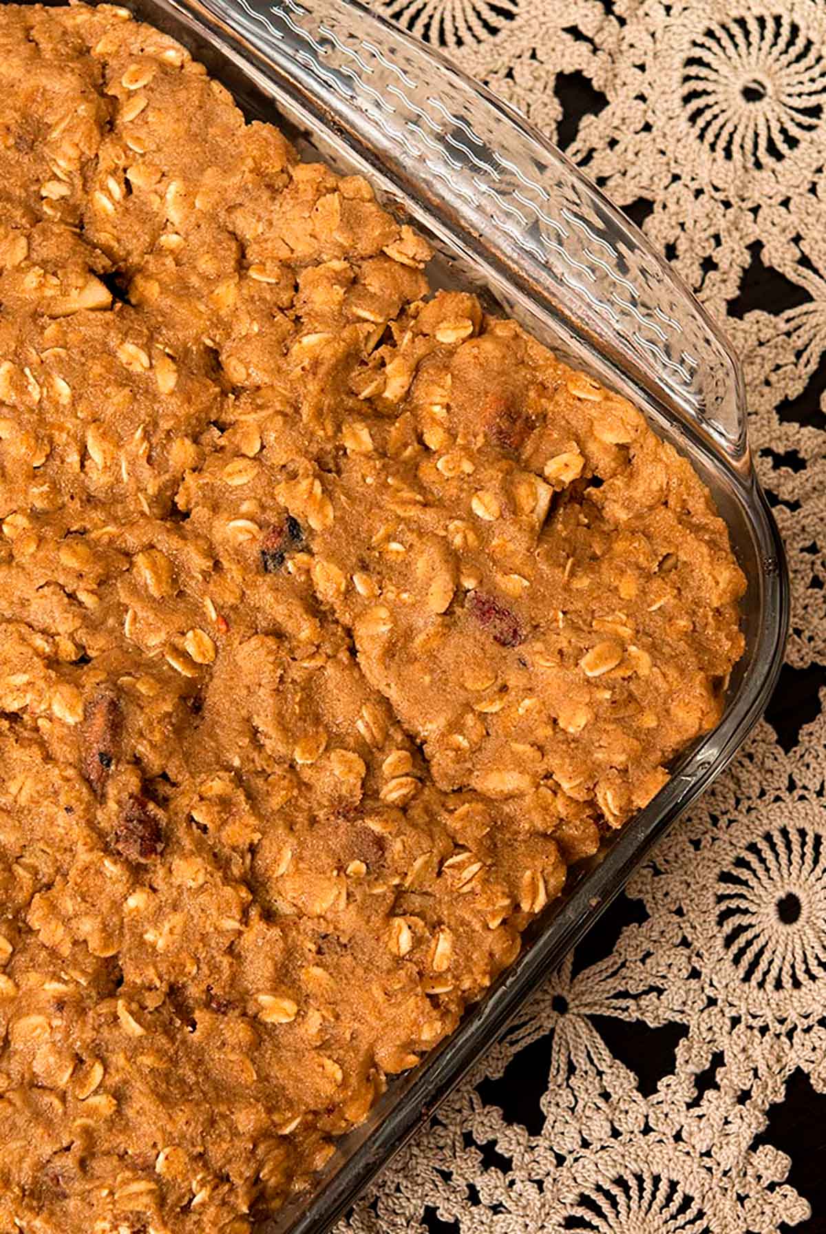 A pyrex full of uncooked cranberry apple crisp on a table with an antique table cloth.