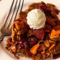 Cranberry apple crisp on a plate, topped with whipped cream and sprinkled with marigold flower petals.