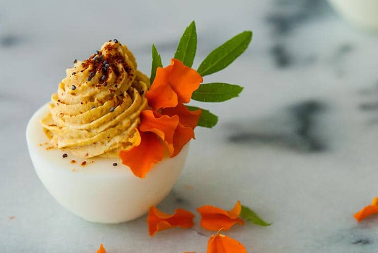 A deviled egg on a marble plate, garnished with flower petals and a sprig of green leaves.
