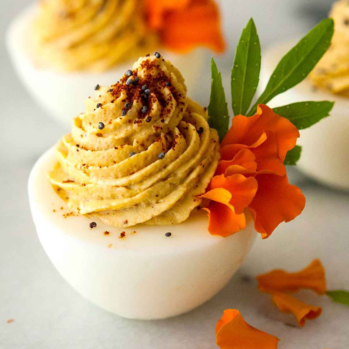 Deviled eggs garnished with marigold petals, spices and leaves on a marble table.