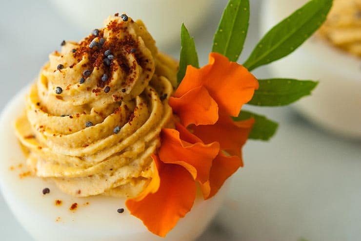 Deviled eggs garnished with marigold petals, spices and leaves on a marble table.