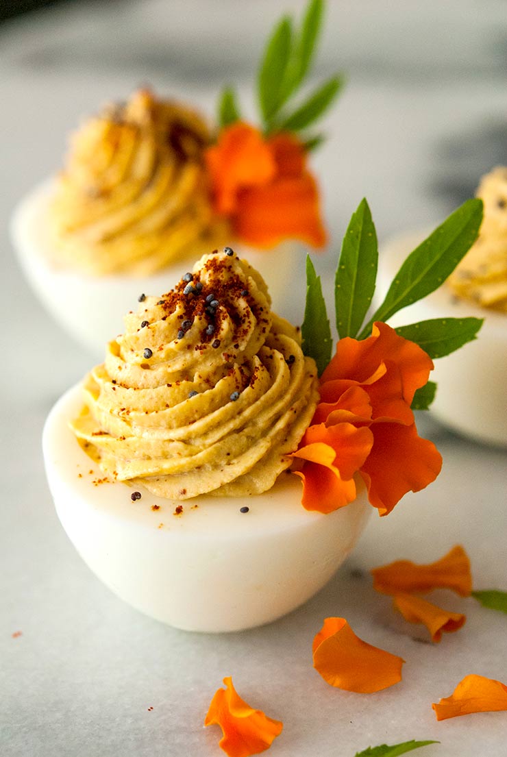 Deviled eggs garnished with marigold petals, spices and leaves on a marble table.