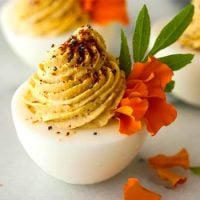 Deviled eggs garnished with marigold petals, spices and leaves on a marble table.