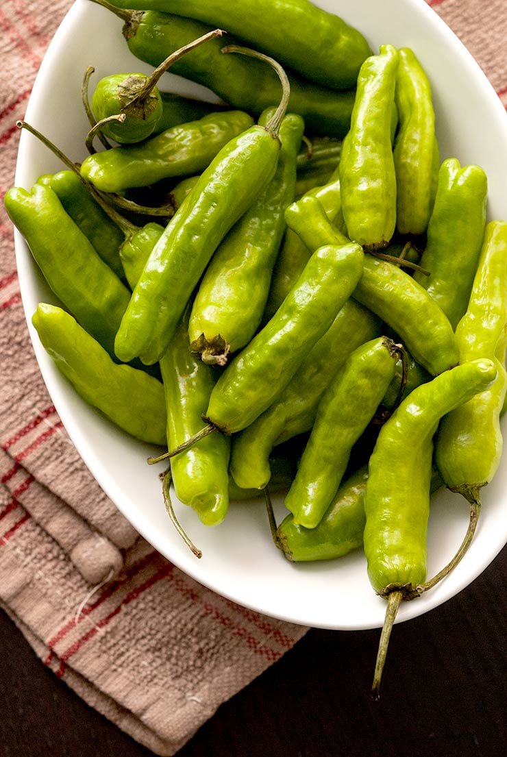 Fresh shishito peppers in a bowl on a folded napkin.