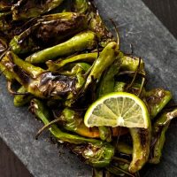 Blistered shishito peppers on a slate with a lime slice.