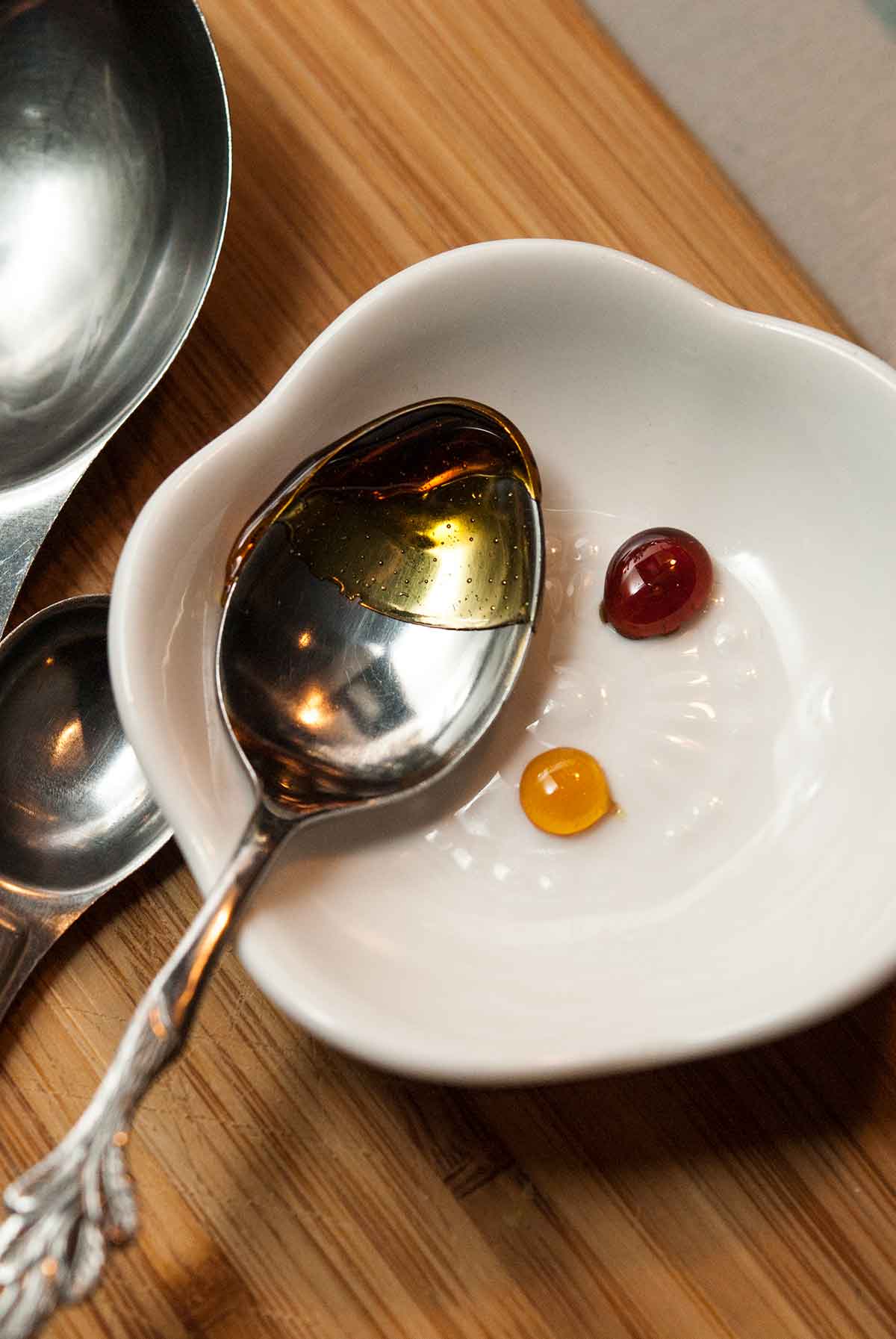 2 different color drops of caramel on a small white plate with a spoon.