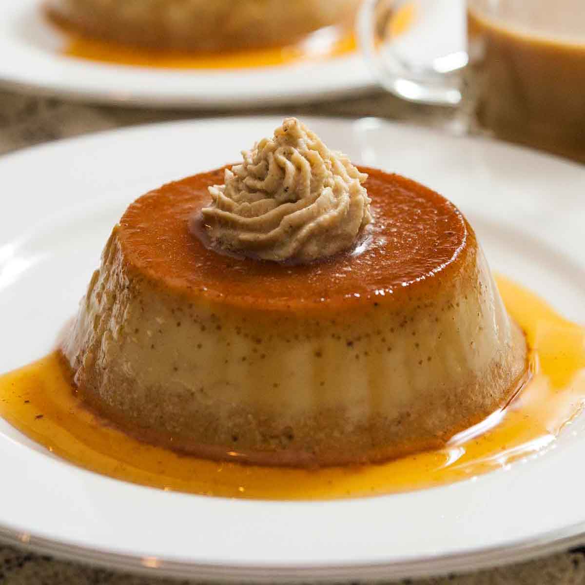 2 pumpkin flans on plates on a table, topped with chai whipped cream, with a small cup of coffee.