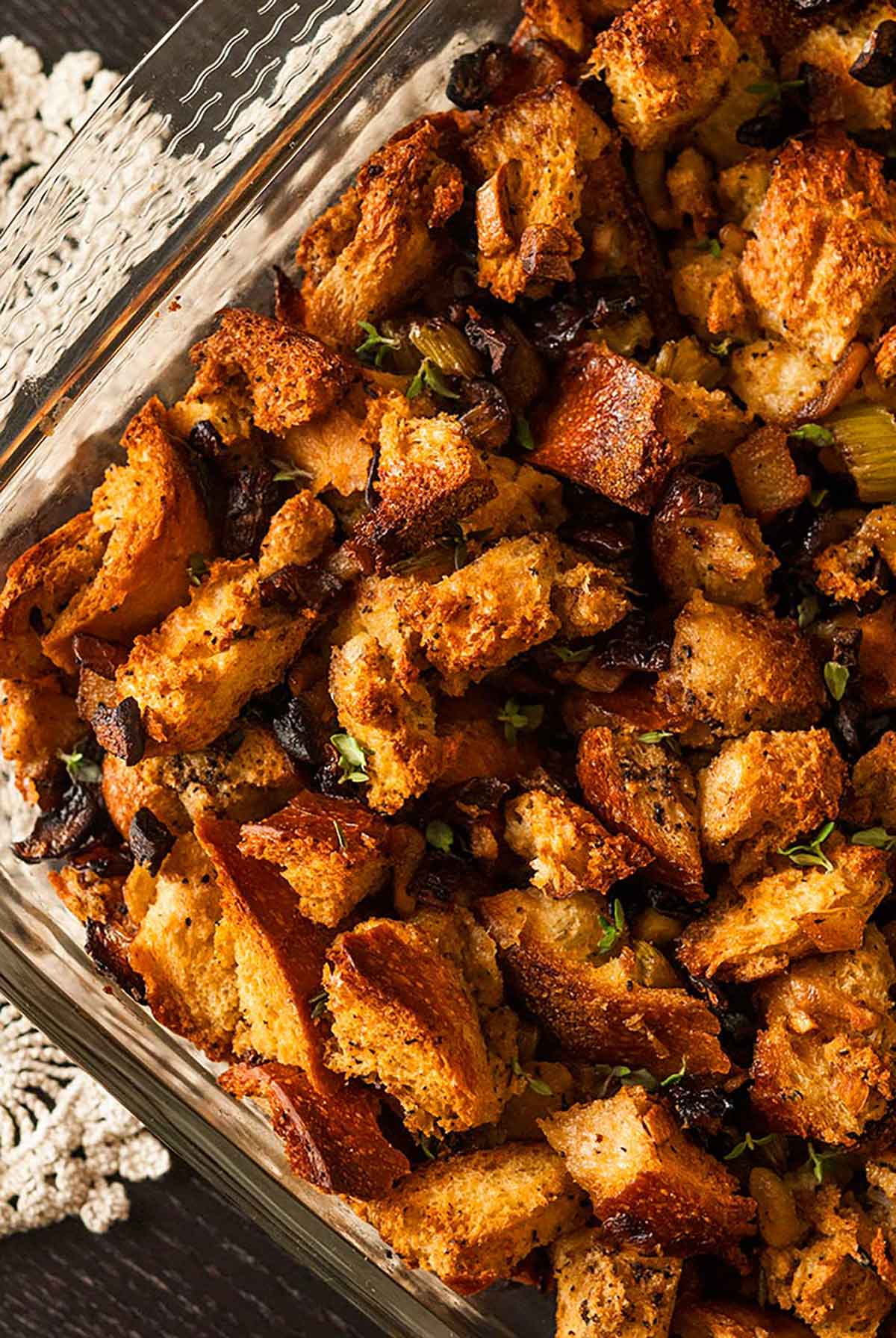 This traditional homemade bread stuffing recipe is moist and crunchy, flavorful and packed with earthy herbs and spices. The very best stuffing for turkey, duck, chicken or Cornish game hen! #stuffing, #recipes A pyrex baking dish with stuffing on a table with a lace cloth underneath.